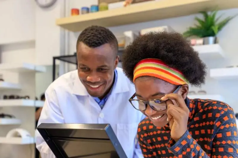 A smiling optician helping a female patient choose a new pair of eyeglasses in the bright and welcoming Optical Department at KELH.